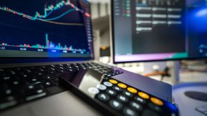 Computador com tela em gráficos da bolsa de valores e celular em aplicativo de calculadora