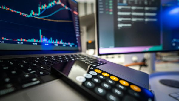 Computador com tela em gráficos da bolsa de valores e celular em aplicativo de calculadora