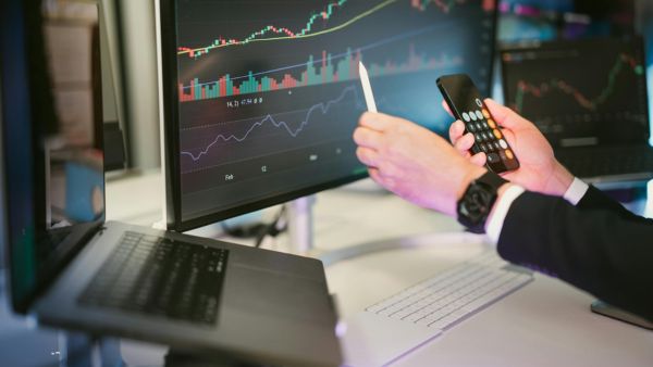 Investidor acompanhando variação de ação no computador e calculadora aberta no celular
