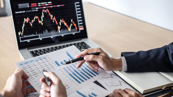 Investidores analisando dados de empresa enquanto olham preço de ativo através de home broker de distribuidoras