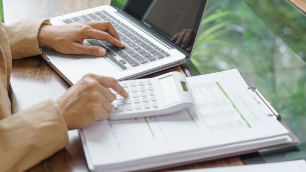 Investidor analisando dados da empresa e usando calculadora e laptop para verificar overhead