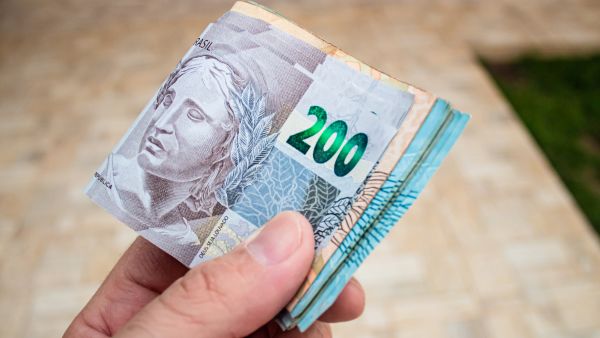 Investidor segurando diversas notas de reais na mão