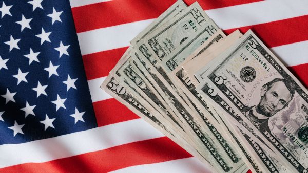 Notas de dólar com bandeira dos Estados Unidos ao fundo representando o investimento de renda fixa em dólar