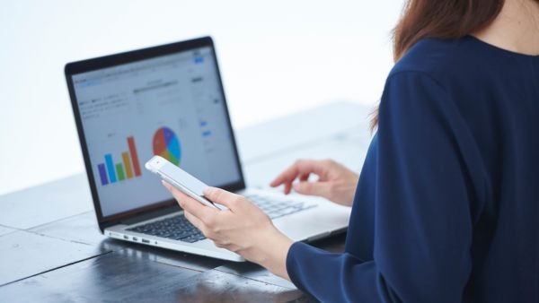 Investidora analisando dados de empresa antes de investir em IPO usando notebook e celular