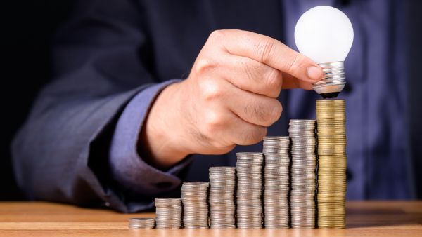 Investidor colocando lâmpada no topo de montes de moedas em ordem crescente representando o crescimento de patrimônio com investimentos