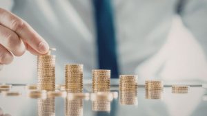 Investidor fazendo pilhas de moedas em cima de mesa representando ganhos graduais com operações de arbitragem