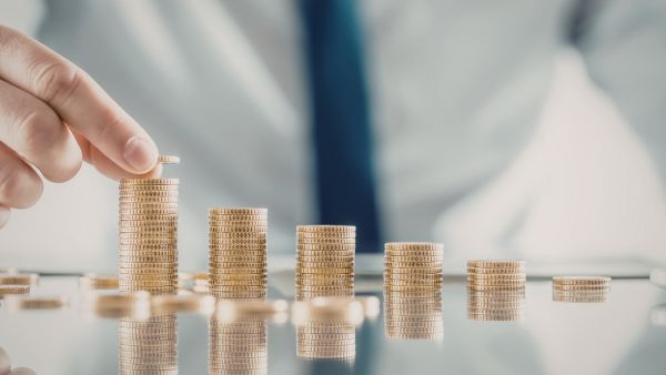 Investidor fazendo pilhas de moedas em cima de mesa representando ganhos graduais com operações de arbitragem