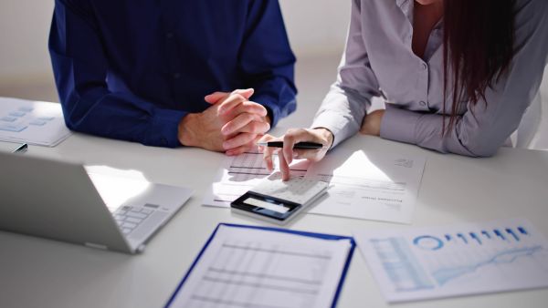 Perito contador fazendo perícia contábil com informações da empresa e auxiliar ao lado