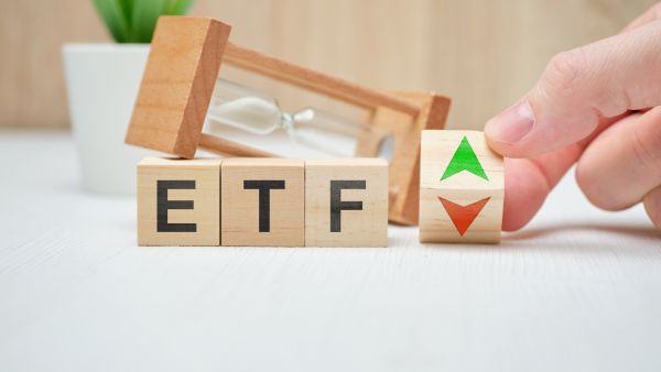 Pessoa colocando blocos de madeira ao lado de ampulheta em superfície representando o funcionamento de ETFs