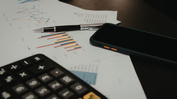 Calculadora, dados de empresa e celular representando o uso de princípios contábeis para demonstrações financeiras