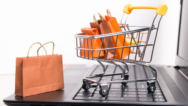 Carrinho de compras com sacolas em miniatura em cima de notebook representando o uso de GMD para avaliar crescimento de ecommerce