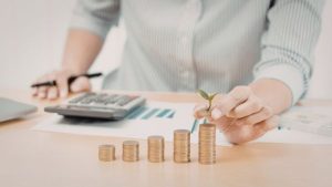 Investidor com dados de empresa e calculadora para avaliar ativo e pilhas de moedas na frente representando pensamento estratégico