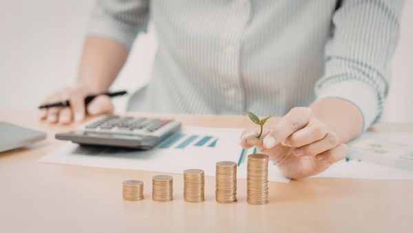 Investidor com dados de empresa e calculadora para avaliar ativo e pilhas de moedas na frente representando pensamento estratégico