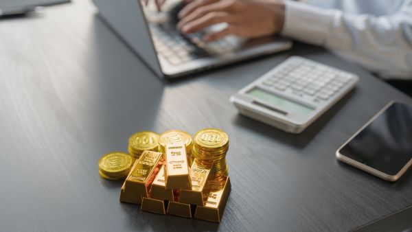 Investidor trabalhando no computador com barras e moedas de ouro ao lado representando investimento em ouro pelo GLD