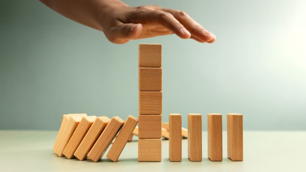 Pessoa impedindo efeito dominó em peças de madeira com solução inteligente representando o conceito de stop loss